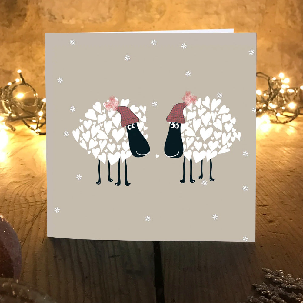 Snuggly Sheep Christmas card on a wooden table with warm fairy lights