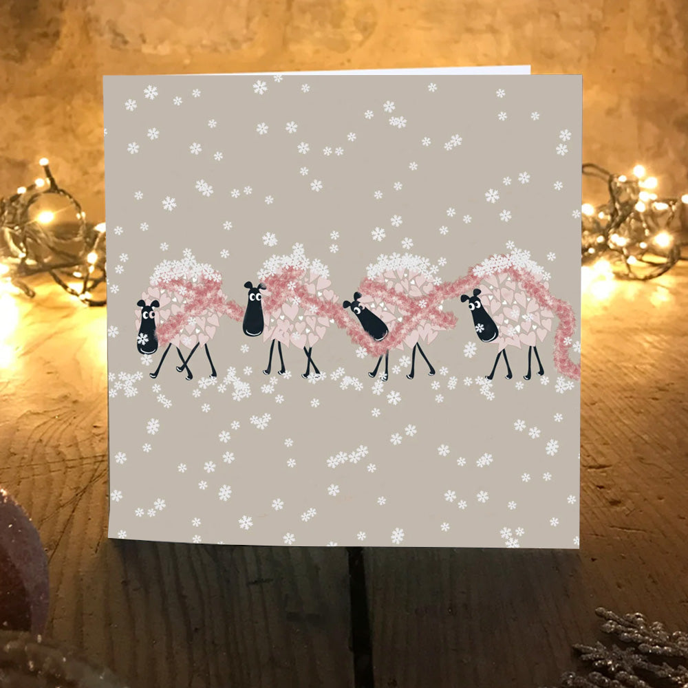 Snuggly Sheep Christmas card on a wooden table with warm fairy lights