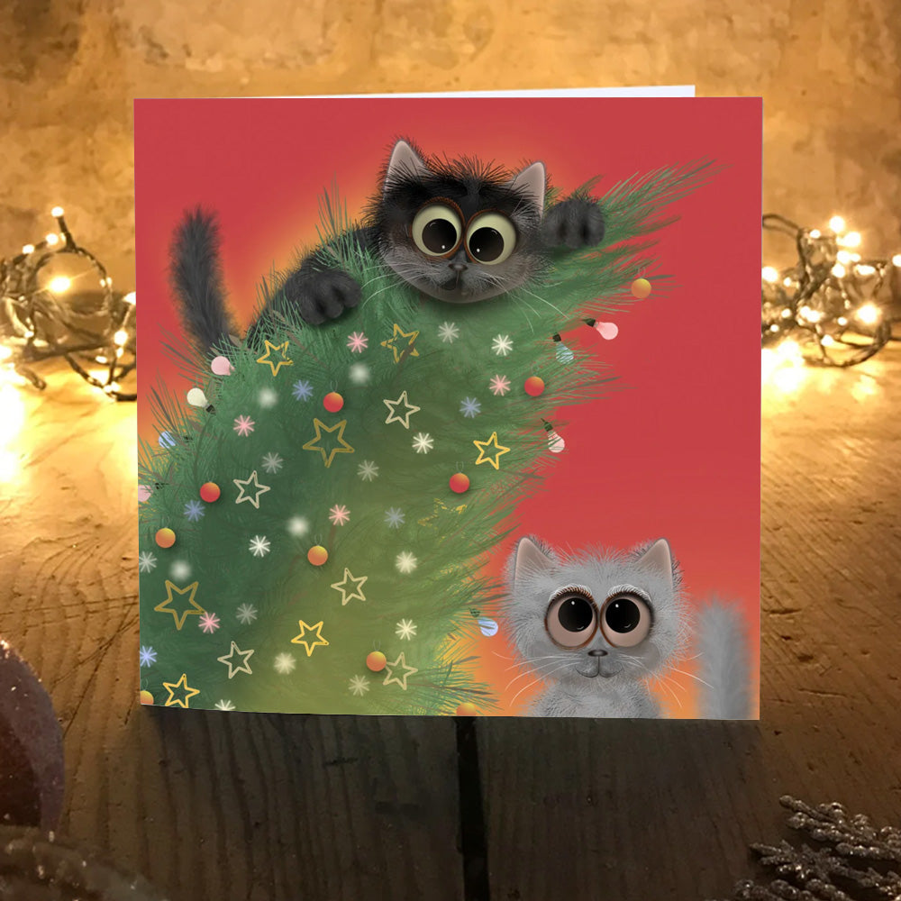 Catastrophe Christmas card with two kittens wrecking the tree, on a wooden table with fairy lights