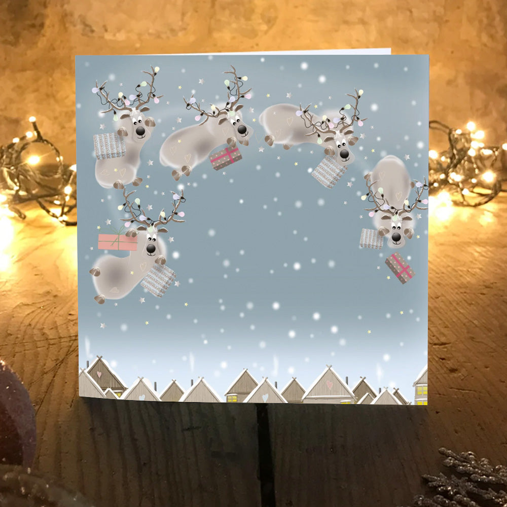 Landing Gear card design, O'Dears reindeer flying with wrapped presents above a snowy village