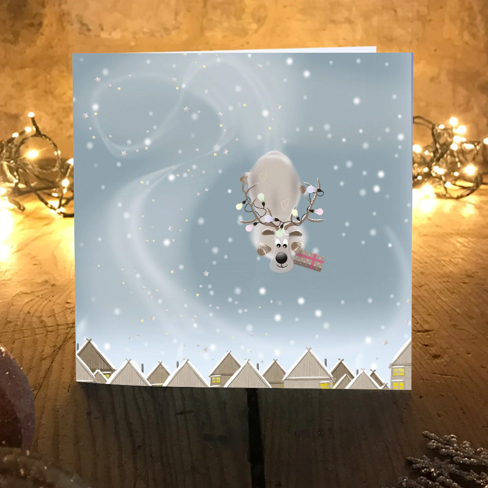Steer Clear card design, O'Dears reindeer swooping down through falling snow carrying a pink-ribboned present